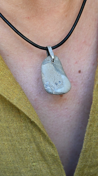 Close-up of a necklace with a stone pendant on a person wearing a yellow garment.