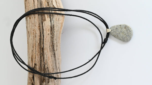 Black cord necklace with a gray stone pendant on a wooden stick. Summer vibes