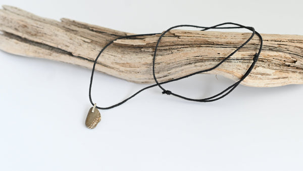 Necklace with a seashore pebble pendant on a black cord, placed on a piece of driftwood against a white background.