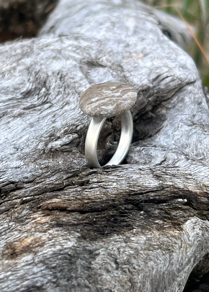 Handmade Silver ring with seaside pebble on a textured wooden surface