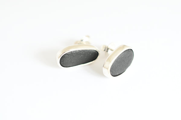 A pair of oval stud earrings with dark textured stones and silver bezel settings, shown on a plain white background.