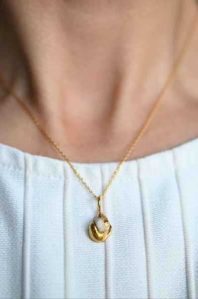 neck wearing a delicate gold chain necklace with a small abstract gold pendant.