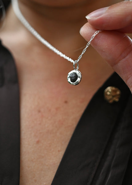 a silver chain necklace with a small, textured circular pendant with rough seashore stone 