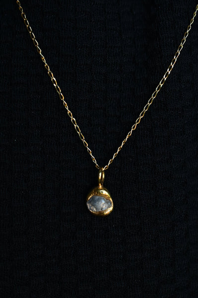 A gold plated chain necklace with a small, rough-cut grey stone pendant in a gold setting, displayed against a black knit background.