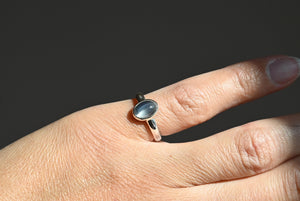 Silver ring with a moonstone on a person's finger against a dark background