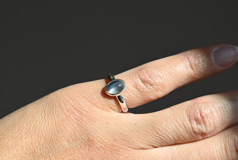 Silver ring with a moonstone on a person's finger against a dark background