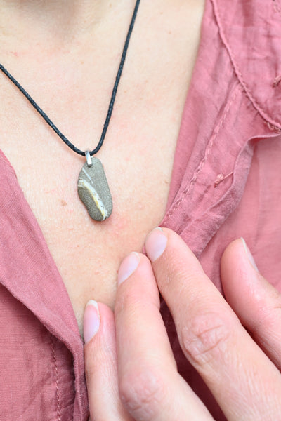 Close-up of a person wearing a small sheashore pebble , attached to a black string.