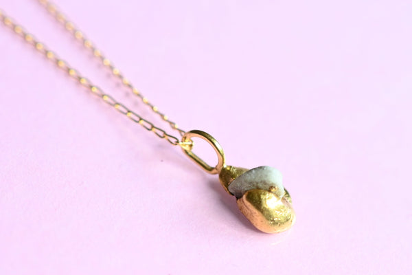 A gold chain necklace with a small pendant featuring a textured gold bead and a white seashore pebble stone.